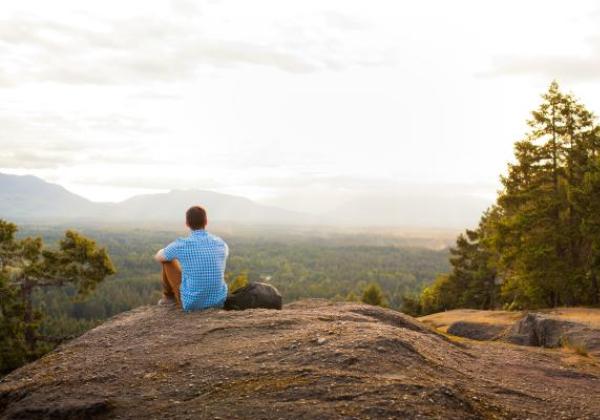 Student sitting on a mountain looking at horizon